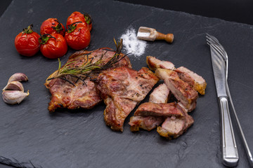 pork steak on black slate and grilled tomatoes and salt