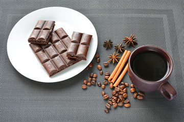 fragrant cup of coffee with porous chocolate among coffee beans, star anise and cinnamon sticks on a dark background