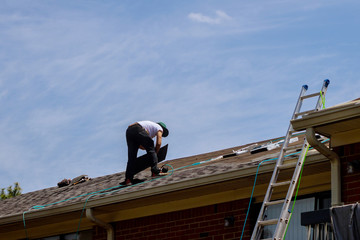 Roof repair, worker with replacing gray tiles shingles on house