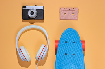 Hipster outfit. Skateboard with headphones, audio cassette on yellow color background. Creative fashion minimalism. Trendy retro 80s style. Minimal summer fun. Music concept. Top view