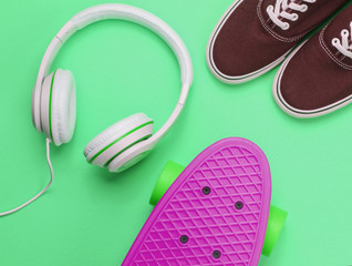 Hipster fashion look. Skate, sneakers, headphones on green background. Top view. Flat lay