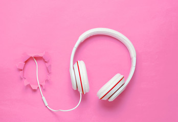 White classic wired headphones on pink background with a torn hole. Retro style. Minimalistic music concept. Top view.