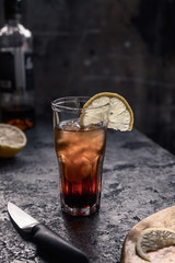 A glass of whiskey with cola full of ice with a slice of lemon on a dark background and copy space. Alcoholic cocktail