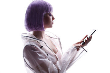 Beautiful woman with purple hair in futuristic costume with smartphone in her hand. Girl browsing internet on smartphone. White background. Free space for text.