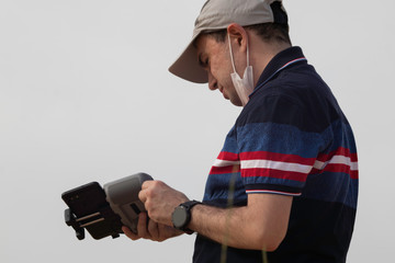 A man flying a drone during the 2020 COVID-19 corona virus outbreak with a surgical mask on his face 