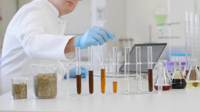 Chemist working with hemp CBD oil in laboratory and writing results in laptop.