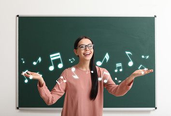 Beautiful music teacher near blackboard in classroom