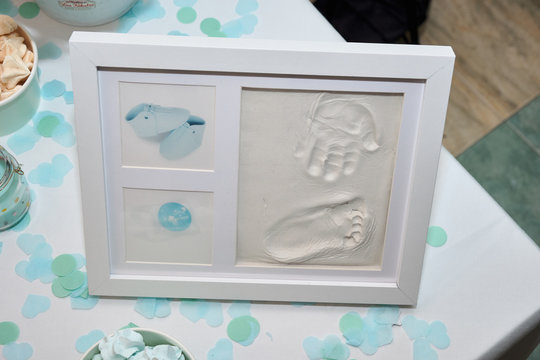 Baby footprint and handprint on clay mold plaque in a frame. To remember in the future how small the baby was. Cute frame images cheerful childhood celebration event. Baby DIY keepsake to keep forever
