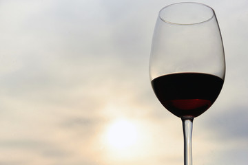 Close-up of a glass glass of red wine against a blurred background of the sky and sunset in the evening. Concept of romantic holidays