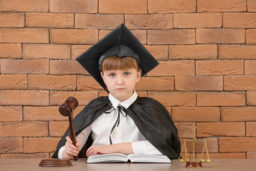 Portrait of little judge sitting at table against brick background