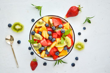 Bowl of vegetarian fresh fruit salad of different fruits: banana, kiwi, apple, orange, strawberry, blueberry.The concept of diet, proper nutrition, fitness diet. copy space. top view