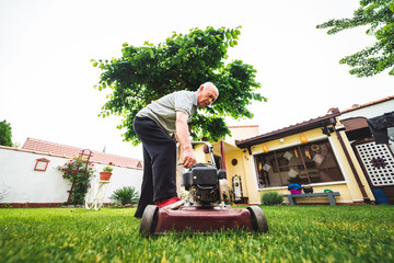 an older man tries to start a lawn mower in the garden, mowing the grass