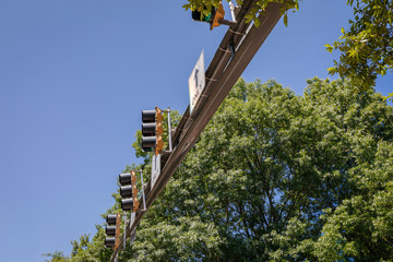 View of overhead traffic signal lights on an extension arm, blue sky and green trees, horizontal...