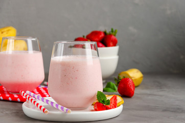 Strawberry smoothie or milkshake with banana in a glass on a gray concrete background. Summer cold drink. Horizontal orientation. Copy space.