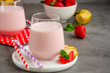 Strawberry smoothie or milkshake with banana in a glass on a gray concrete background. Summer cold drink. Horizontal orientation. Copy space.