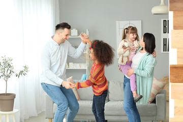 Happy couple with little adopted children dancing at home