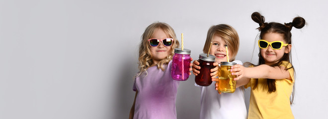 Little male and females in sunglasses, colorful casual clothes. They showing cocktail bottles, smiling, posing isolated on white