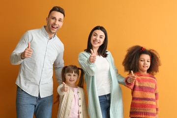 Happy couple with little adopted children showing thumb-up on color background