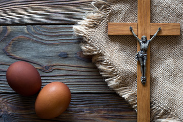 A crucifix and red-painted chicken eggs lie on burlap and wooden boards. Holy Easter.