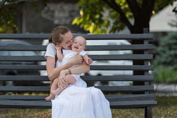 Young mother hugging and kissing baby sitting on Park bench. long-awaited first child