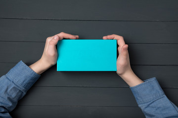 Small blue box in children's hands. Black background. Child holding gift box. Top view.