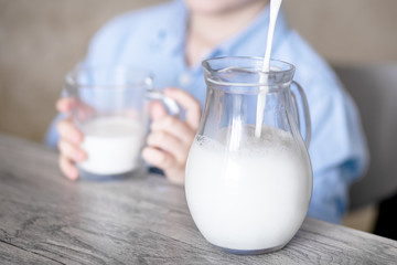 Close-up of a glass jug into which milk spills. Milk flows beautifully in a fine stream.