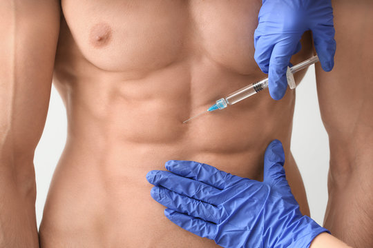 Muscular man receiving injection of steroids on light background, closeup