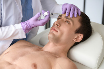 Fototapeta na wymiar Handsome man receiving filler injection in beauty salon