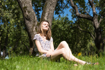 Naklejka na ściany i meble Young attractive happy woman sleeping sitting in a summer garden under a tree