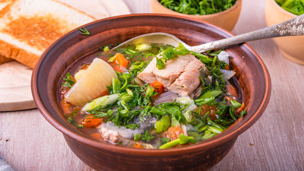 Simple fish soup with salmon and vegetables in a clay bowl