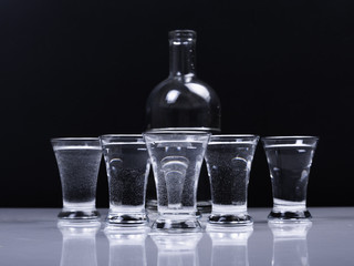 Glasses with vodka and a bottle in the background on a white table and on a black background