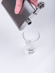 Female hand pours vodka into a glass of metal flask - close-up