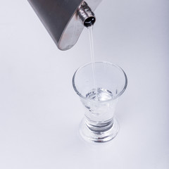 Female hand pours vodka into a glass of metal flask - close-up