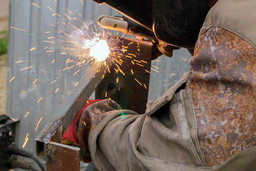 The welder works with metal. Sparks from the welding machine