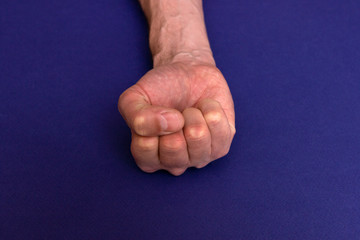 Man hand with large veins on a blue background. fist as a show of strength