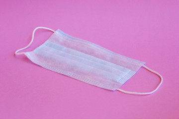 Typical medical mask with rubber ear straps to cover the mouth and nose isolated on a pink background. Protection against viruses and diseases. Covid-19. Pandemic-2020. Healthcare