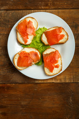 Bruschettas with salmon and cream cheese on a white plate on a wooden table.