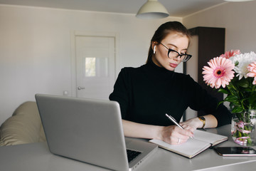 Head shot concentrated young woman freelancer writing notes and planning a day while working at home. Attractive businesswoman studying online.