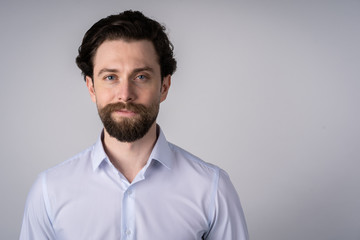 Obraz premium The portrait on the chest young man with a beard in a white shirt, he smiles and looks straight into the camera