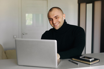 Handsome short haired young caucasian businessman sitting at home office and working on laptop. Home office and remote work concept
