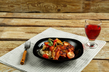 Baked chicken wings in tomato sauce with rice and vegetables on a black plate and a glass of red wine.