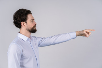 A man with a beard in a white shirt standing on white background and pointing in the direction