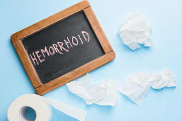 Toilet paper and chalkboard with word HEMORRHOID on color background