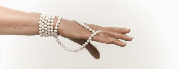 Senior woman hand with Pearl necklace cut out on white. Luxury jewelry on female hand with French manicure. Close up shot. Copy space at right side. Jewelry concept. Toned image