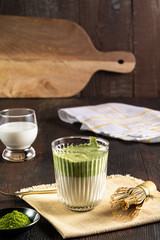 Matcha green tea latte with matcha powder and bamboo whisk on wood background.