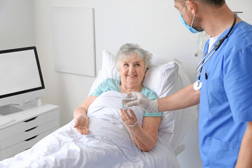 Male doctor working with elderly patient in hospital room