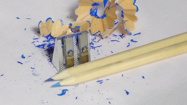 A plain pencil and chrome sharpener with wood shavings on white surface