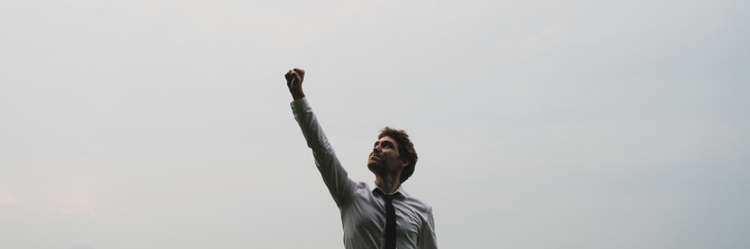 Wide view image of successful young businessman standing under cloudy sky