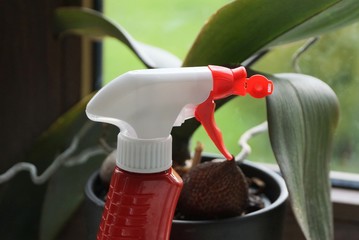 red white plastic bottle with sprayer on a background of green leaves of a plant in a flowerpot in...