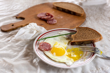 Breakfast. Fried eggs of two eggs and green feathers of onions. Sausage and bread on a wooden board. Sprigs of blossoming apple tree in a crystal vase. Crumpled napkin.